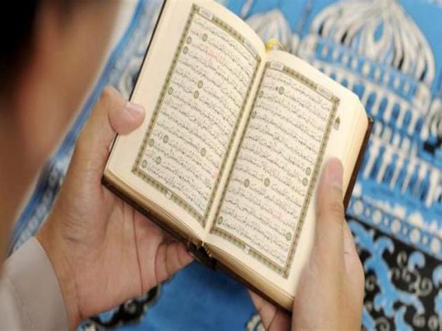 شخص يصلي ويحمل في يده المصحف الشريف